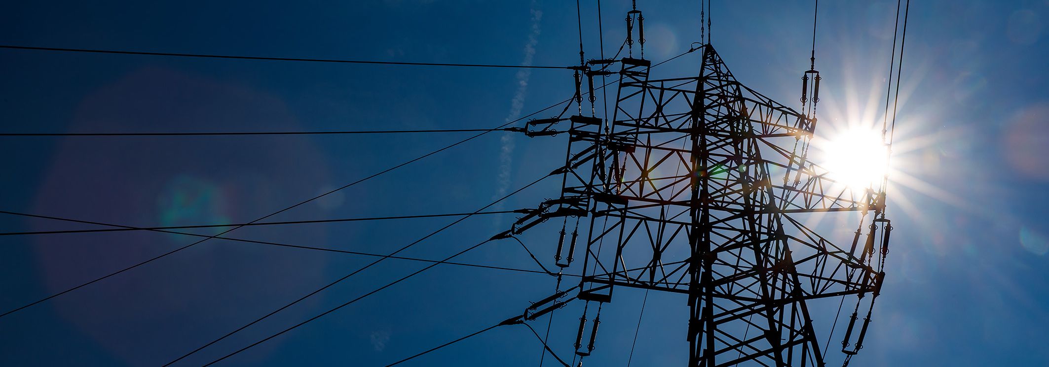 Strommasten vor blauem Himmel und Sonne