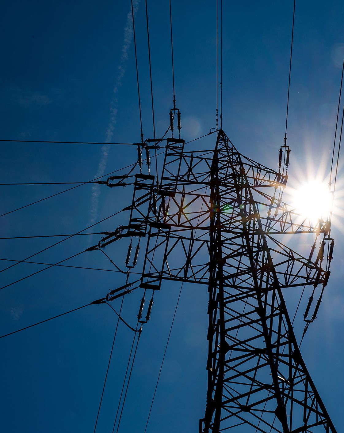 Strommasten vor blauem Himmel und Sonne