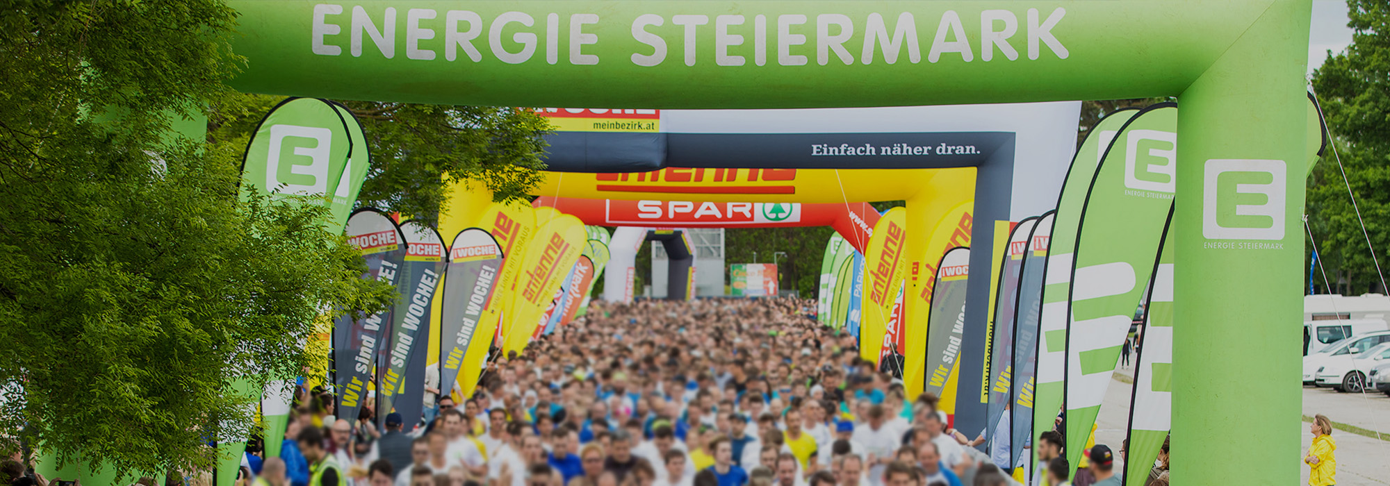 Bei einer Laufveranstaltung stehen über hundert Menschen im Startbereich, während aufblasbare Werbebögen darüber zu sehen sind.