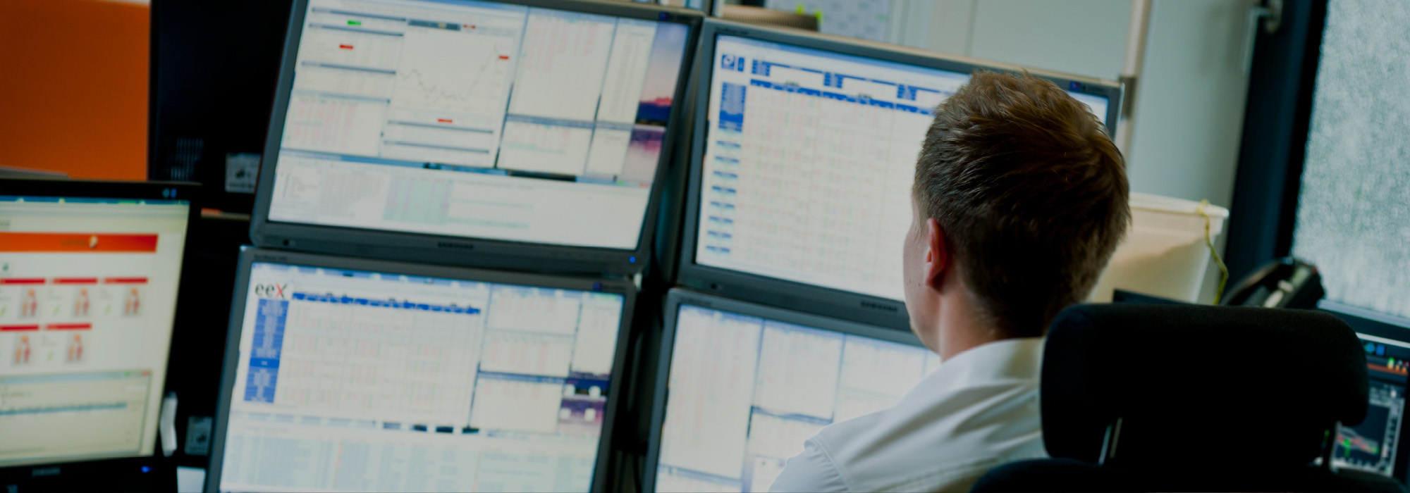 Ein Mann sitzt vor sechs Bildschirmen, auf denen viele Zahlen zu sehen sind.