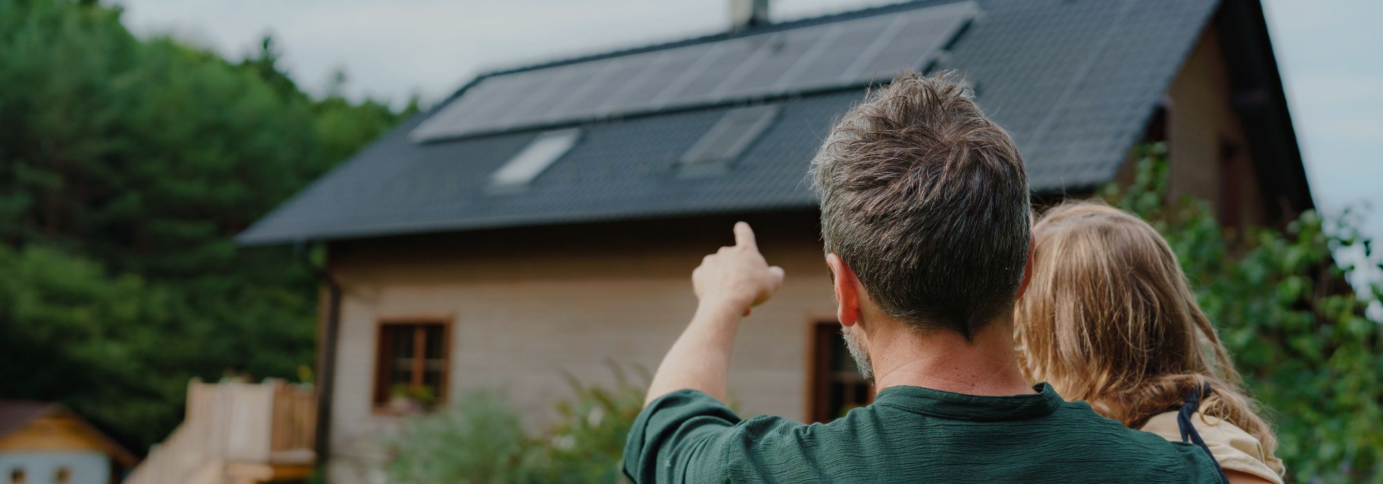 Mann zeigt auf Photovoltaik-Anlage am Dach eines Hauses