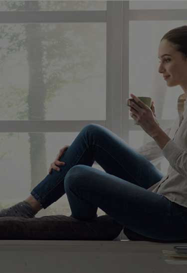 Frau sitzt mit einer Tasse in der Hand am Fenster