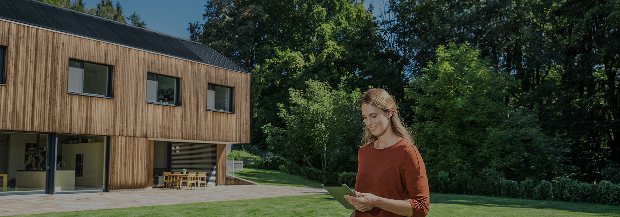 Frau mit Tablet in der Hand steht vor einem Haus